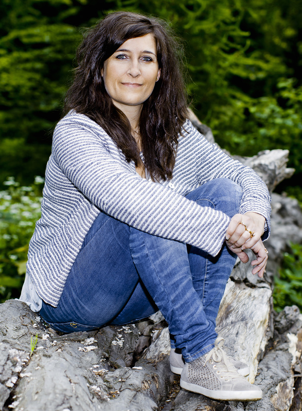Portræt af Marie-Louise Munk, stifter af Monora, siddende på en væltet træstamme i en grøn skov